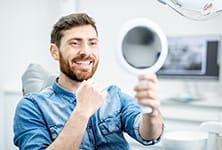 man admiring his smile in a hand mirror 